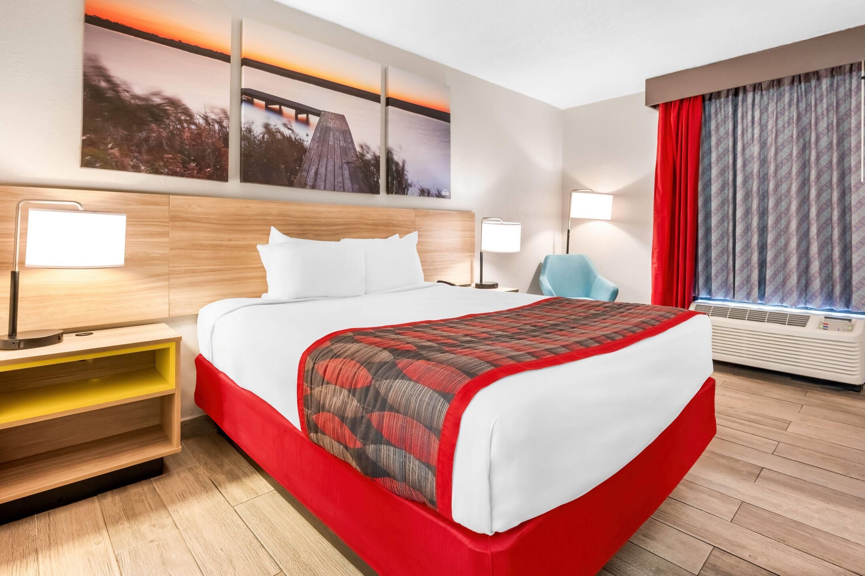 A hotel room with a large bed, two bedside tables, a chair, a desk, and a window with curtains.