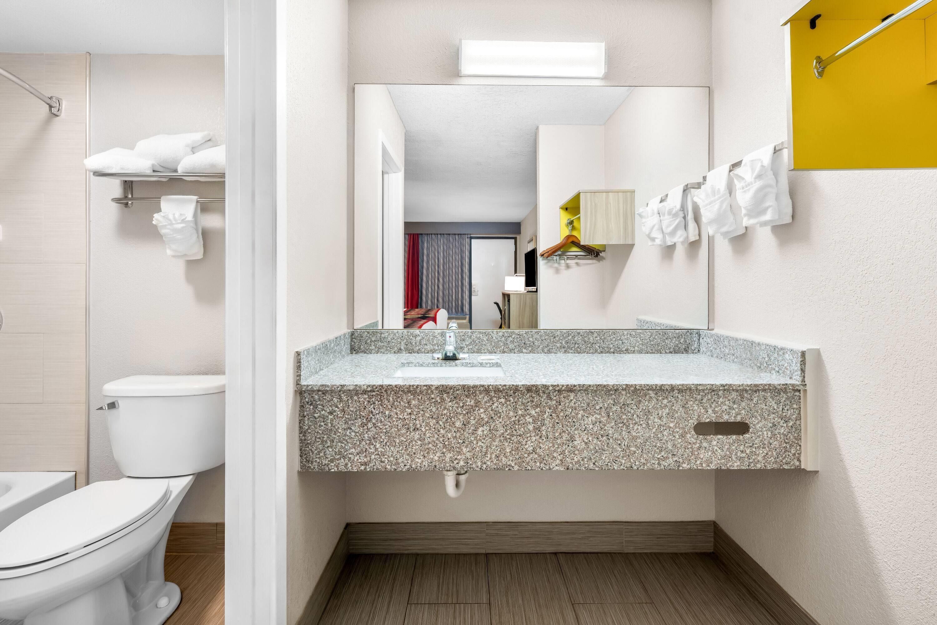 Een moderne badkamer met een wastafel met een granieten blad, een spiegel erboven en een handdoekrek met witte handdoeken.