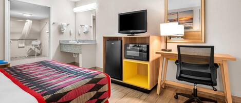 Ein Hotelzimmer mit einem Bett, einem Schreibtisch mit Computer, einem Fernseher, einem Spiegel und einem sichtbaren Badezimmer durch eine offene Tür.