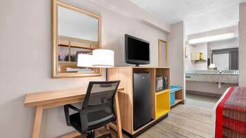 Ett hotellrum med ett skrivbord i trä, en svart kontorsstol, en tv, ett minikylskåp och en säng med ett rött och vitt randigt täcke.