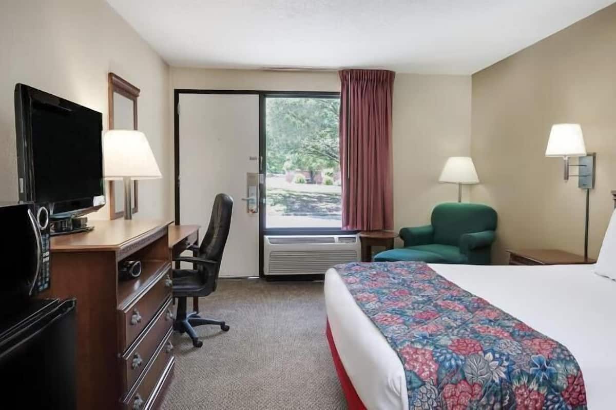 A hotel room with a bed, desk, chair, TV, and a window with curtains.