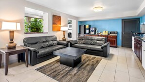 A modern living room with two black leather sofas, a dark coffee table, and a small side table. A kitchen area with a refrigerator, microwave, and cabinets is visible in the background. - Days Inn by Wyndham Hoover Birmingham (Birmingham)