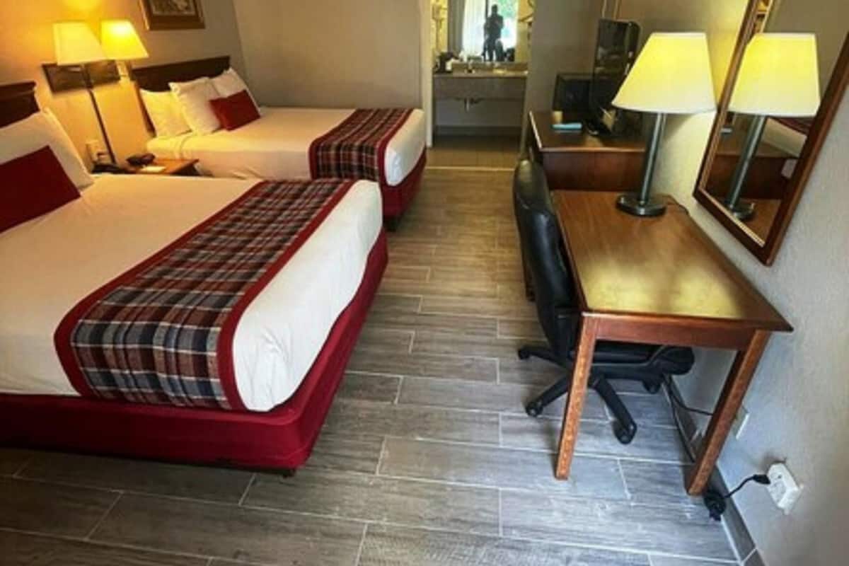 A hotel room with two beds, a desk, and a mirror.