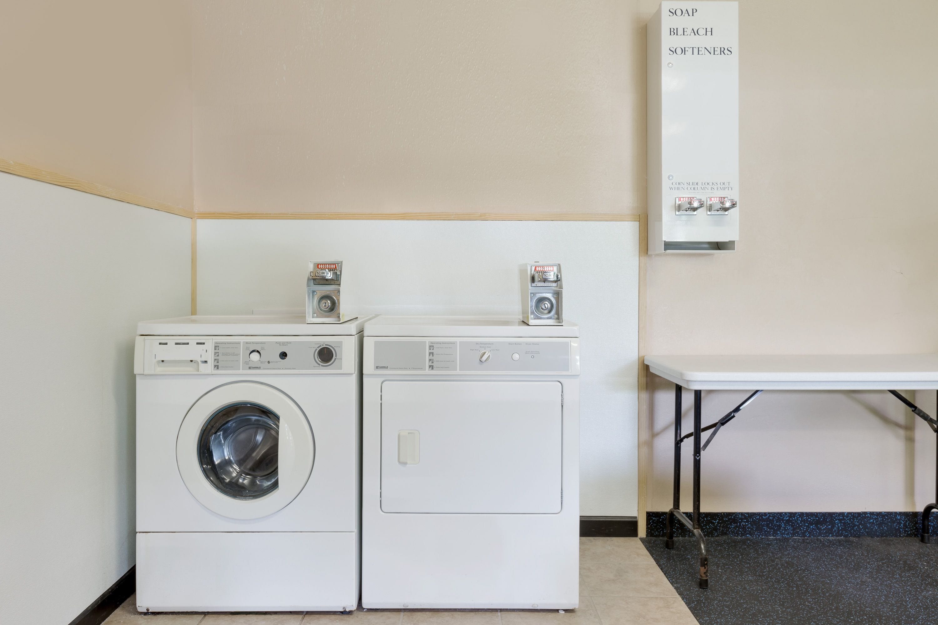 A laundry area with two washing machines and a soap and bleach dispenser.