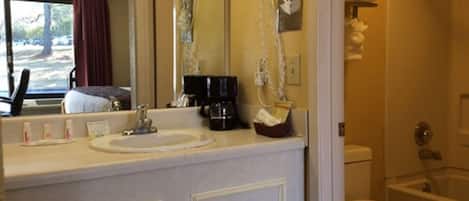 A bathroom with a sink, toilet, and shower. There is a mirror above the sink, and a hairdryer mounted on the wall.