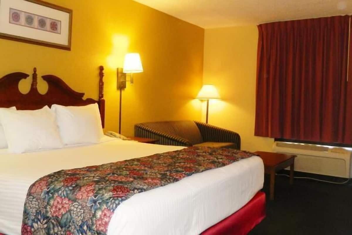 A hotel room with a large bed, two bedside lamps, a chair, a red curtain, and a framed picture on the wall.