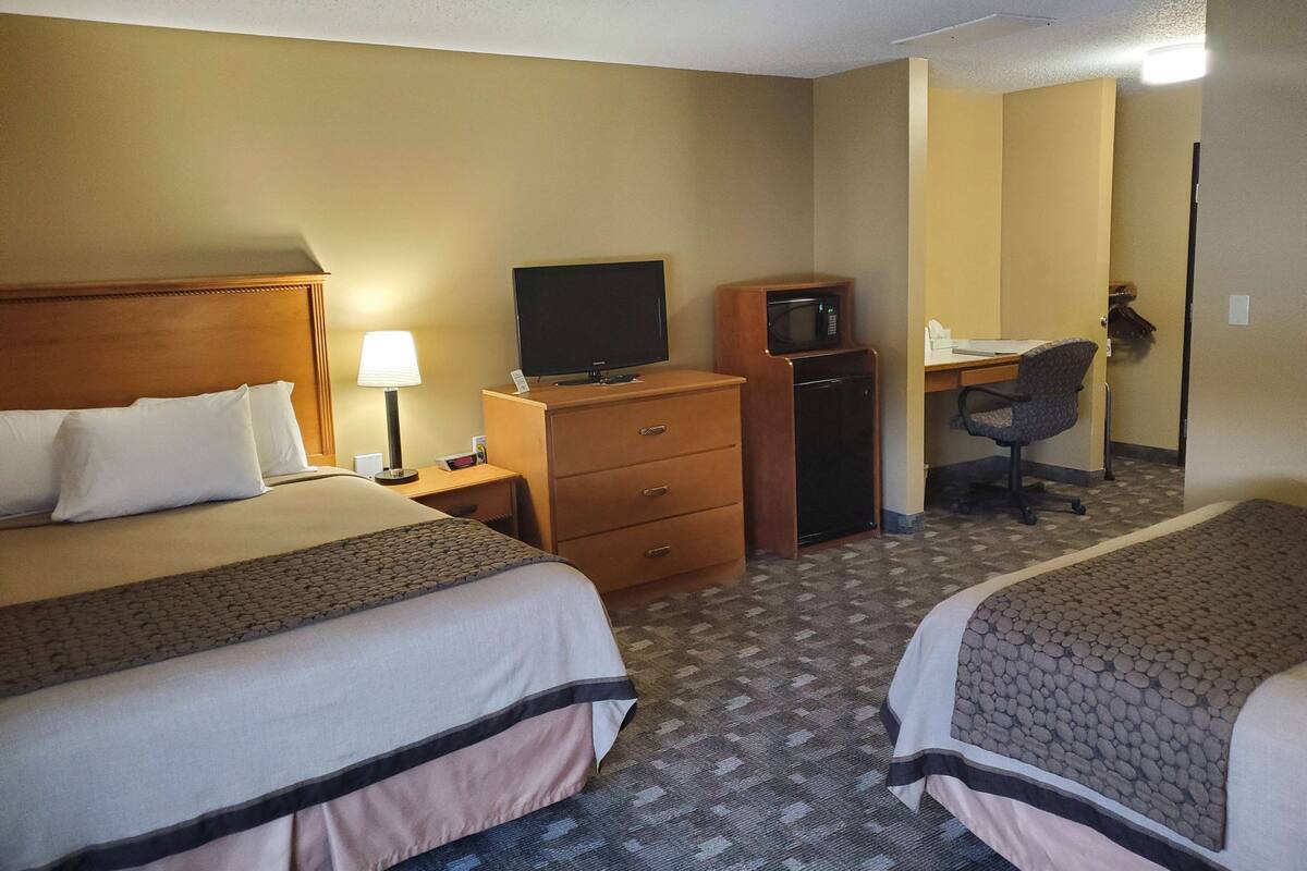 Ein Hotelzimmer mit zwei Betten, einem Schreibtisch mit Computer, einem Fernseher, einer Mikrowelle und einem Sessel.