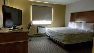 Ein Hotelzimmer mit Bett, Fernseher, Schreibtisch und einem Fenster mit Jalousien.