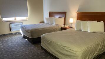 A hotel room with two beds, a nightstand, a lamp, and a window with blinds.