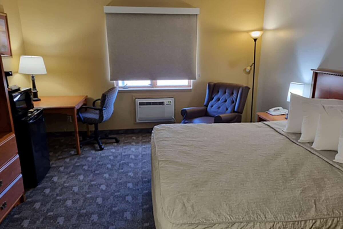 Ein Hotelzimmer mit Bett, Schreibtisch, Stuhl, Lampe, Heizung und Nachttisch.