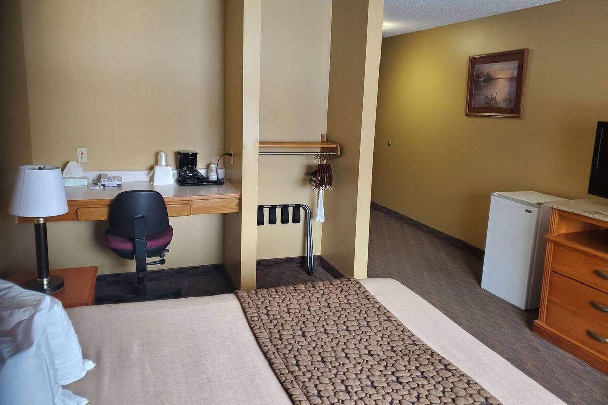 Ein Hotelzimmer mit Bett, Schreibtisch, Stuhl, Lampe, Kaffeemaschine und kleinem Kühlschrank.