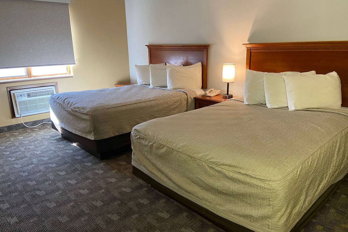 Ein Hotelzimmer mit zwei Betten, einem Nachttisch mit Lampe und einem Fenster mit Jalousien.