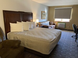 A hotel room with a large bed, a sofa, a chair, a desk, and a window with a view.