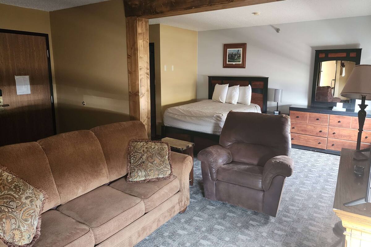 Ein Zimmer mit braun-ledrigem Sofa, braun-ledrigem Sessel, einem Holzschrank und einem Bett mit weißer Bettwäsche.