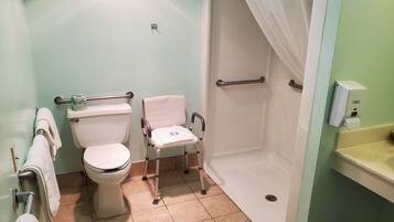 A bathroom with a toilet, a wheelchair, a shower, and a hand sanitizer dispenser.