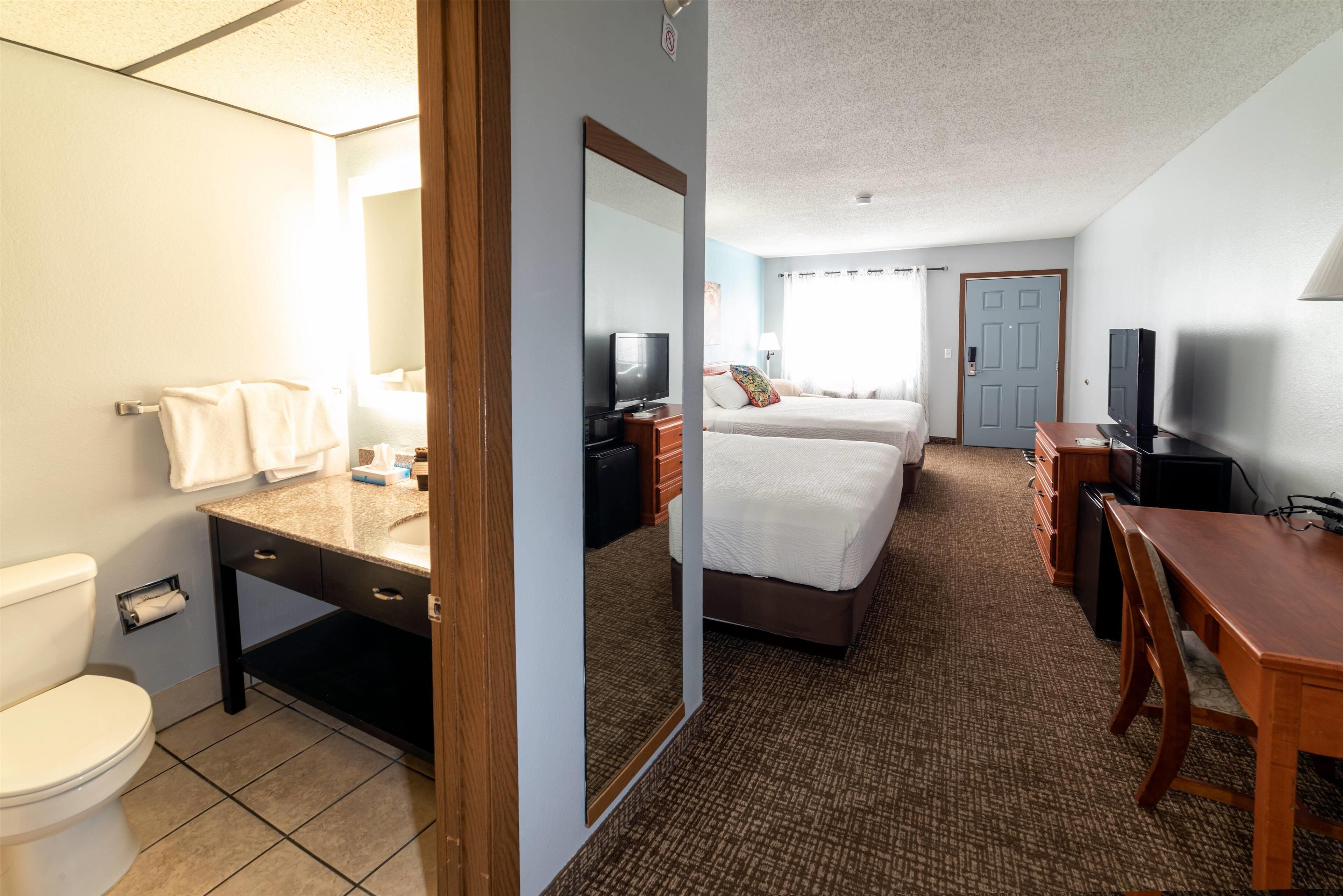 A hotel room with a bathroom, a bed, a desk, and a TV.
