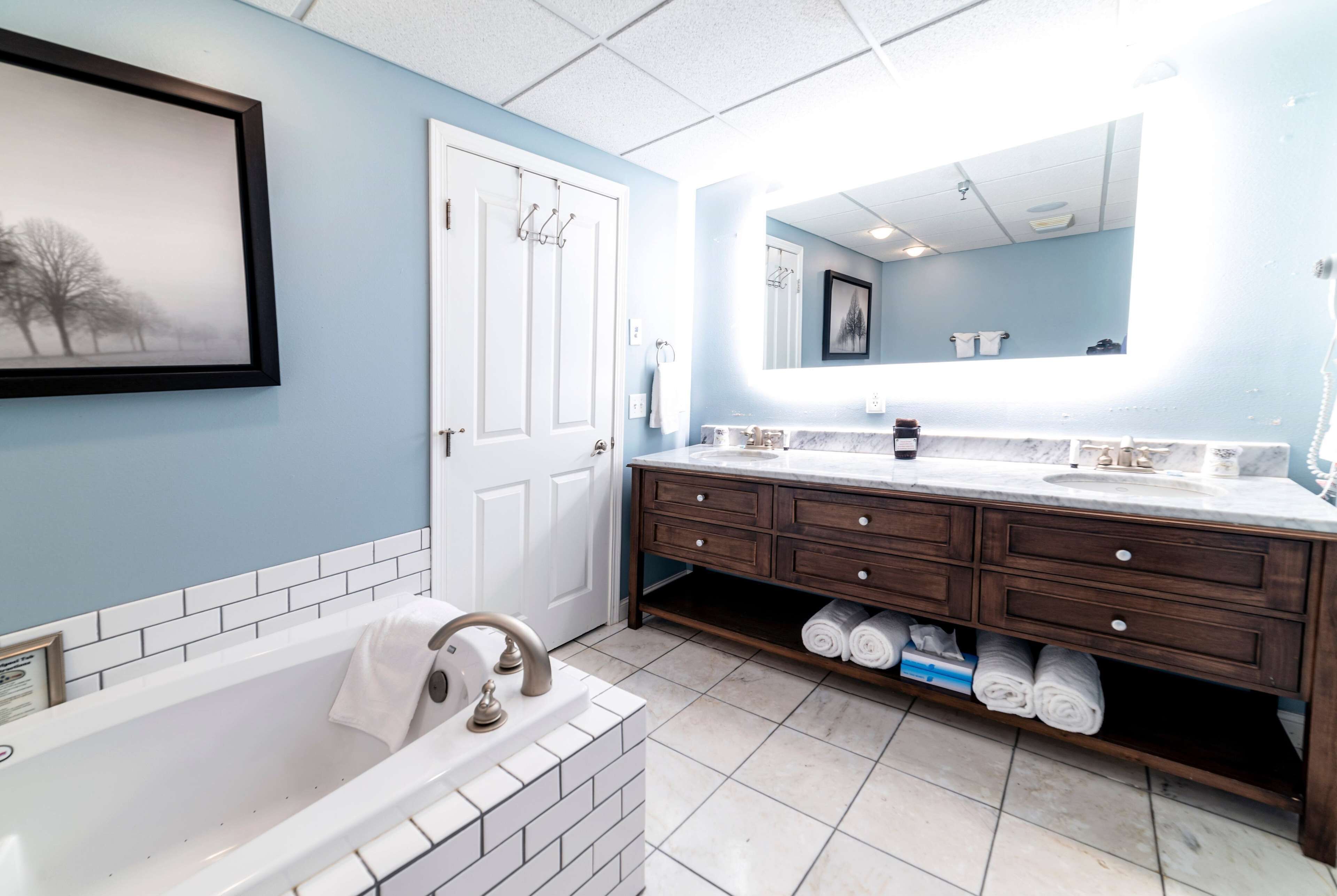 A bathroom with a white bathtub, a double sink vanity with dark wood cabinets, and a large mirror above the sink.