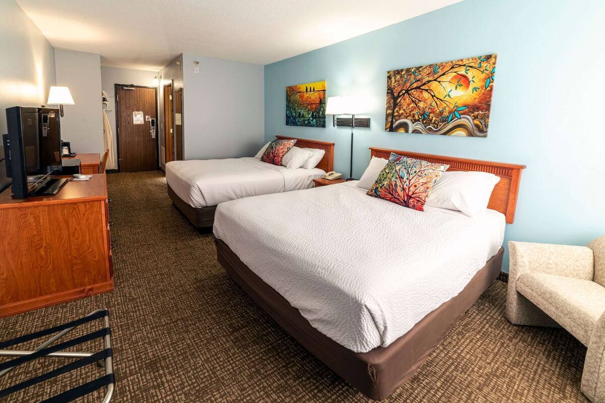 A hotel room with two beds, a desk, a chair, and artwork on the walls.