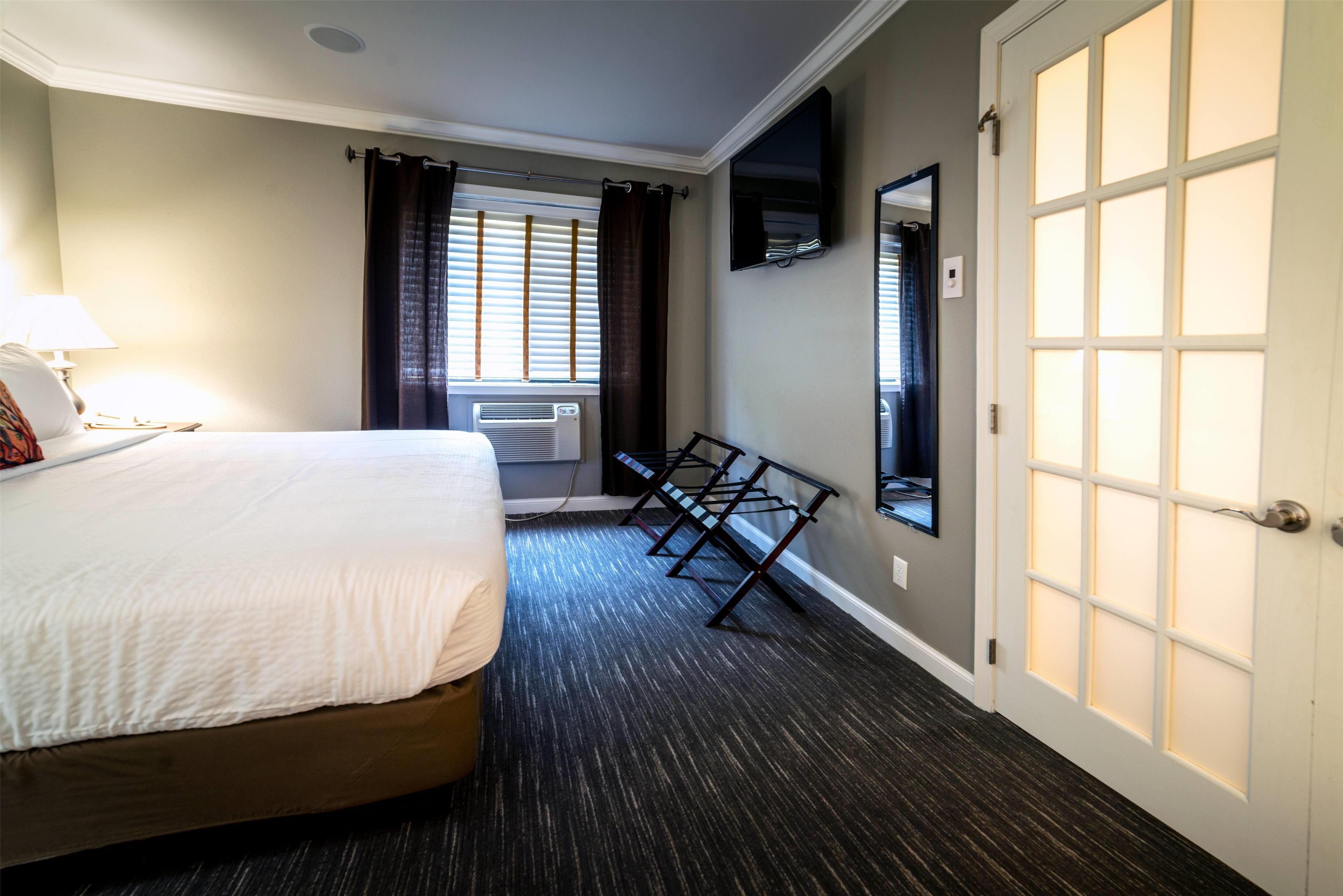 Een hotelkamer met een bed, een aan de muur bevestigde televisie, een raam met gordijnen en een deur met geëtste glaspanelen.