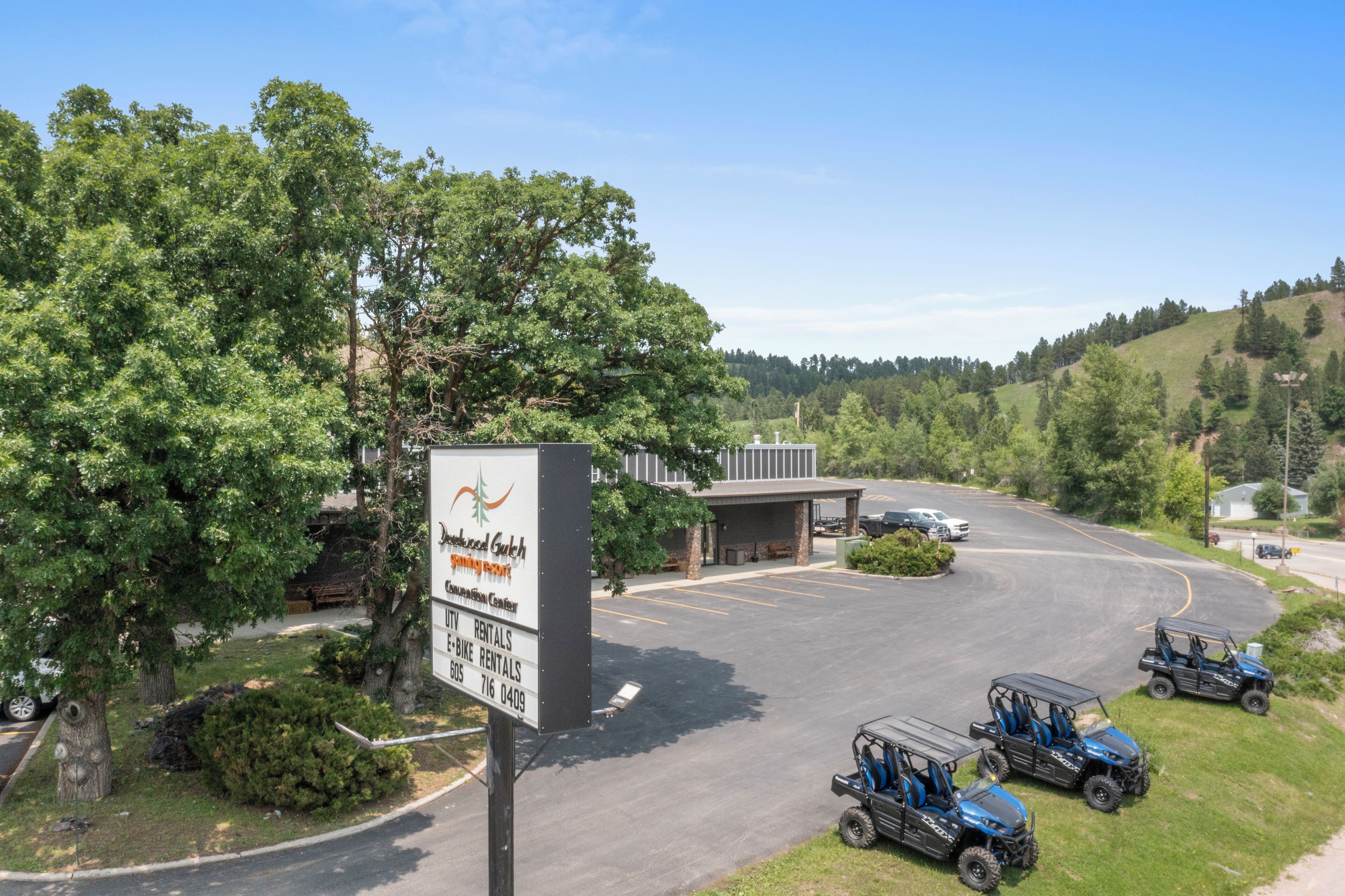 A large outdoor parking area with a sign for a rental center, surrounded by trees and hills.