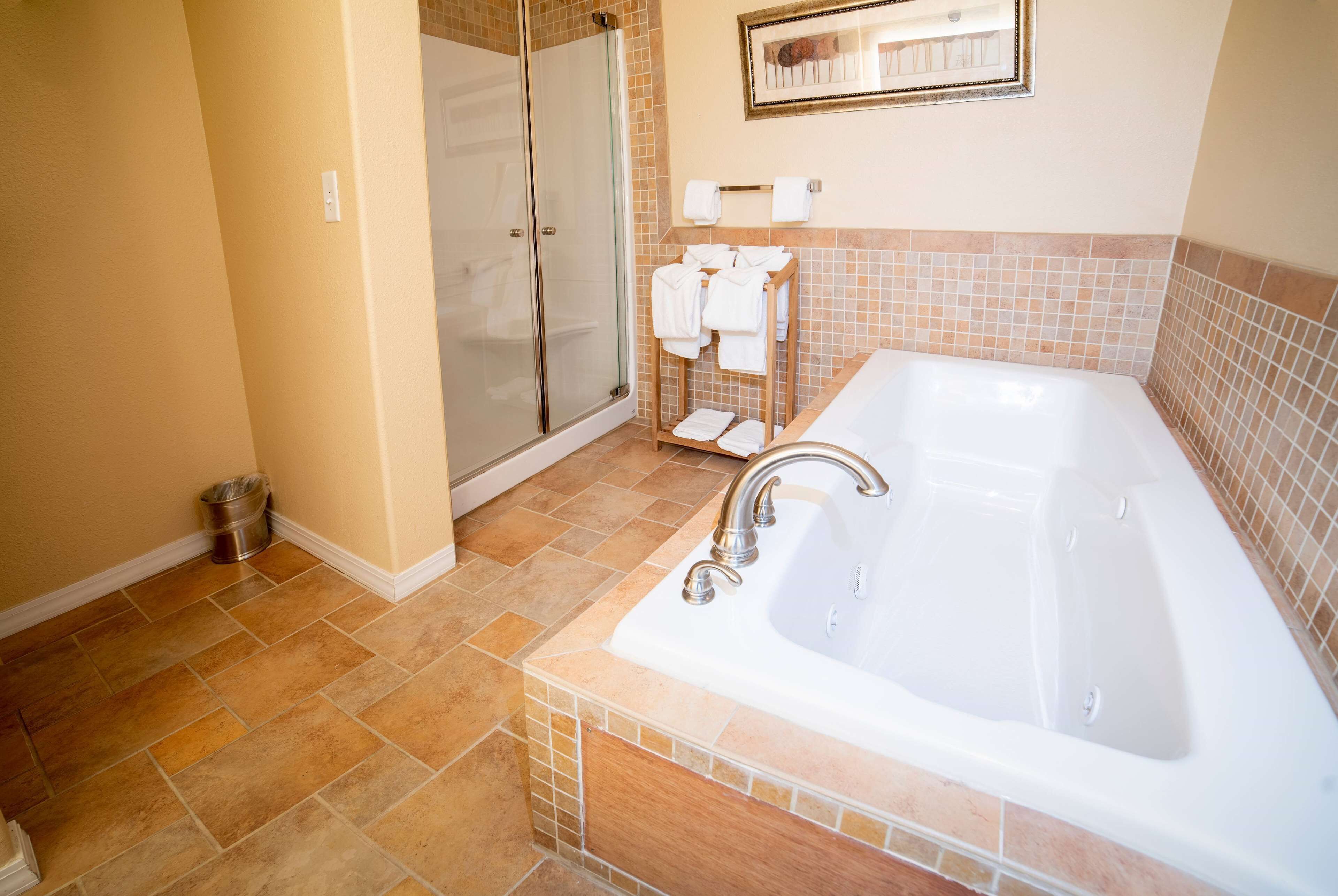Un baño con una bañera grande, cabina de ducha de cristal y un perchero con varias toallas.