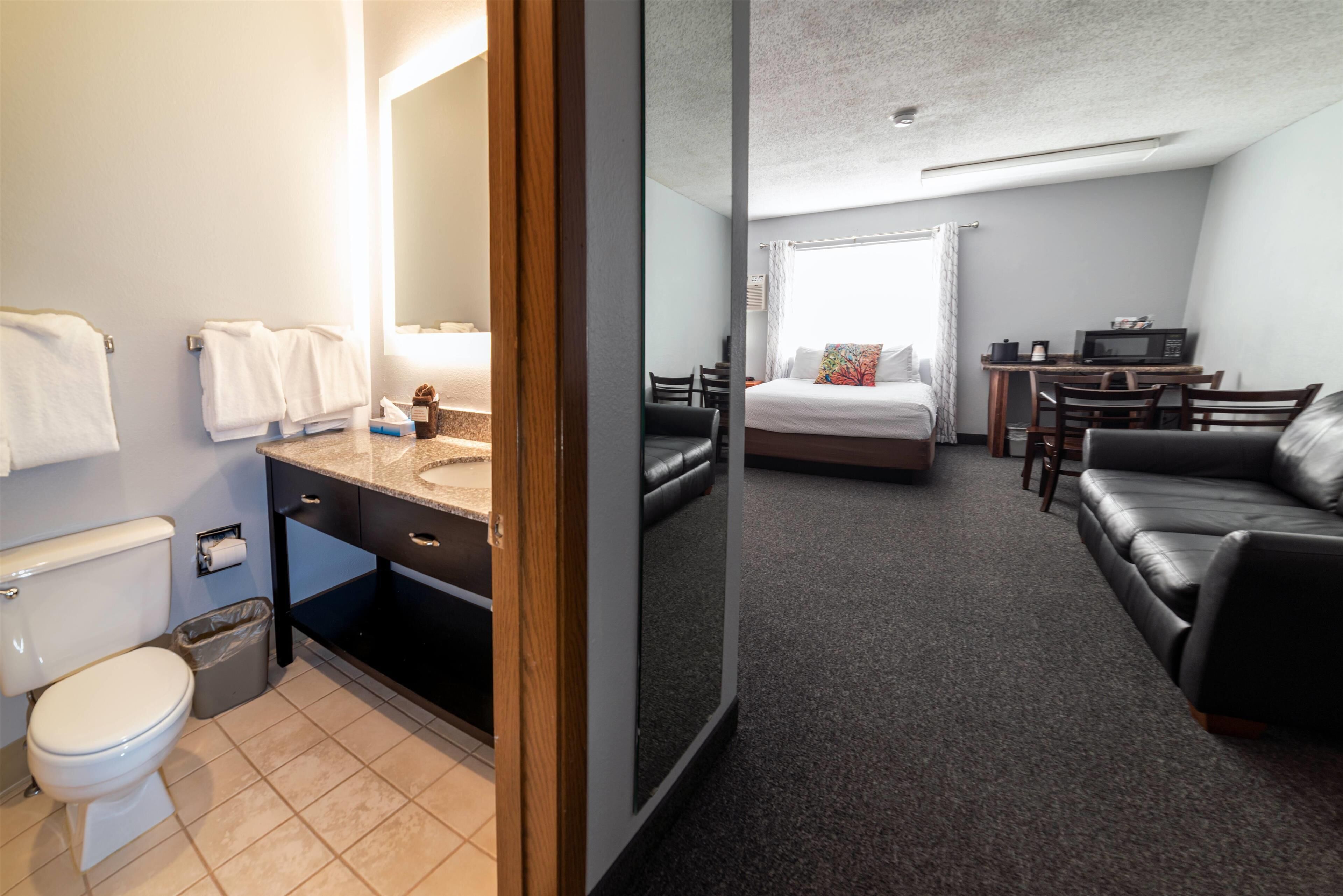 A hotel room with a bathroom, a bed, a desk, and a sofa.
