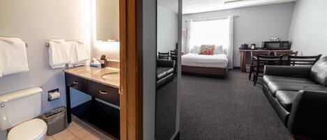 A hotel room with a bathroom, a bed, a desk, and a sofa.