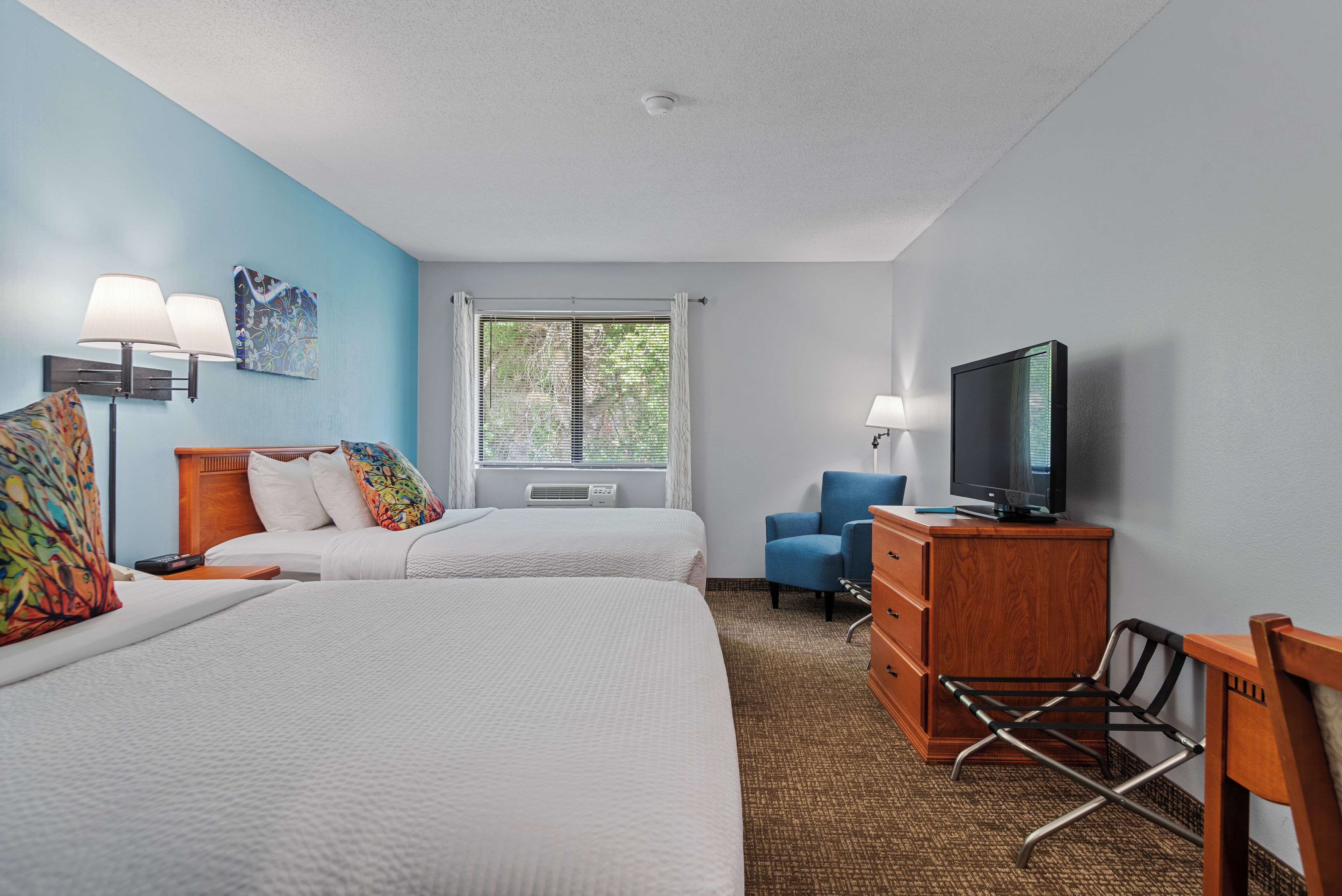 A hotel room with two beds, a TV, a desk, and a chair.