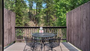 A wooden deck with a round metal table and four chairs, surrounded by a wooden fence and trees.