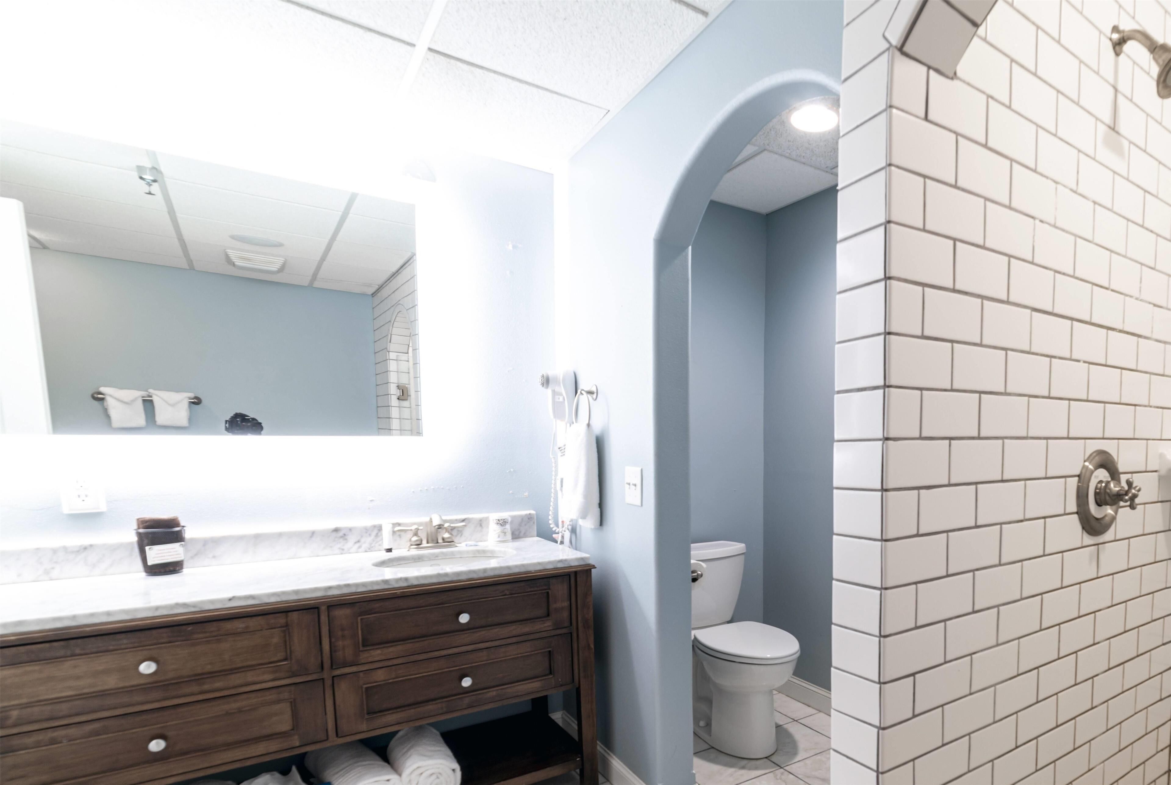 Un baño con lavamanos de mármol, tocador de madera, inodoro y zona de ducha con azulejos.