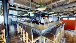 A bar area with a long counter, multiple stools, and hanging green pendant lights. - Riotel Matane (Matane)