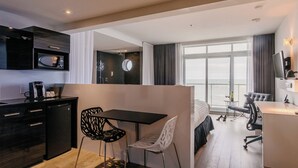 A modern hotel room with a kitchenette, a dining area, a bed, and a large window offering a view. - Riotel Matane (Matane)