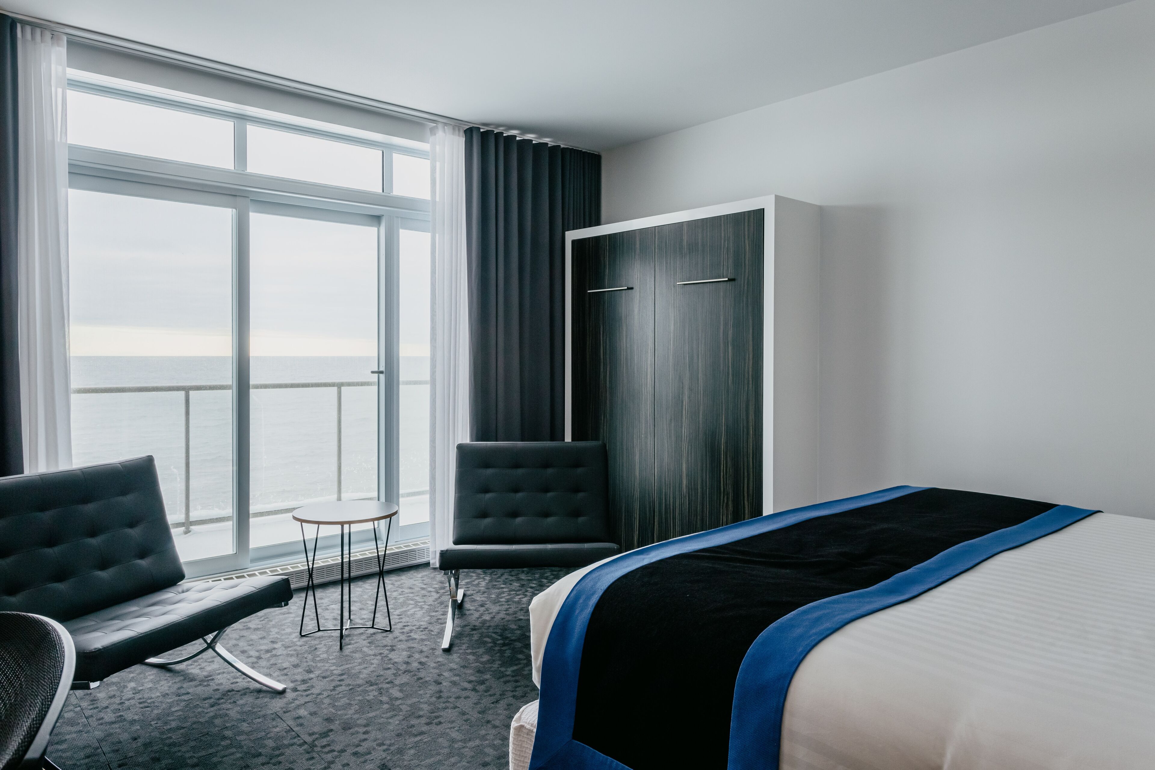 A hotel room with a bed, a chair, a small table, and a wardrobe.