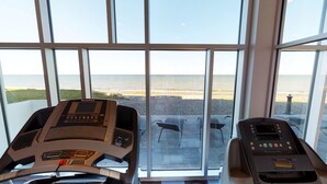 A gym with treadmills and a stationary bike, overlooking a beach. - Riotel Matane (Matane)