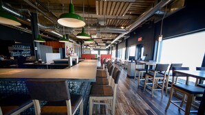 A modern restaurant with a long counter, multiple seating areas, and a view of the outdoors. - Riotel Matane (Matane)