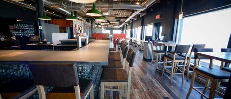 A modern restaurant with a long counter, multiple seating areas, and a view of the outdoors.