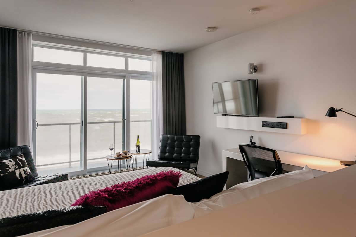 Una habitación de hotel con un ventanal grande, una cama, un televisor, un escritorio y una silla.
