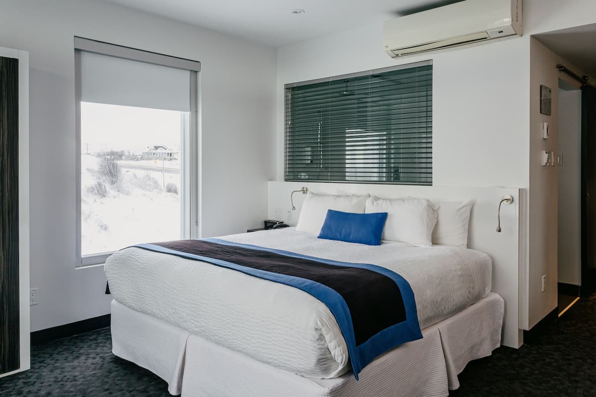 Habitación de hotel con una cama grande, una ventana con persianas, un equipo de aire acondicionado y vistas al exterior.