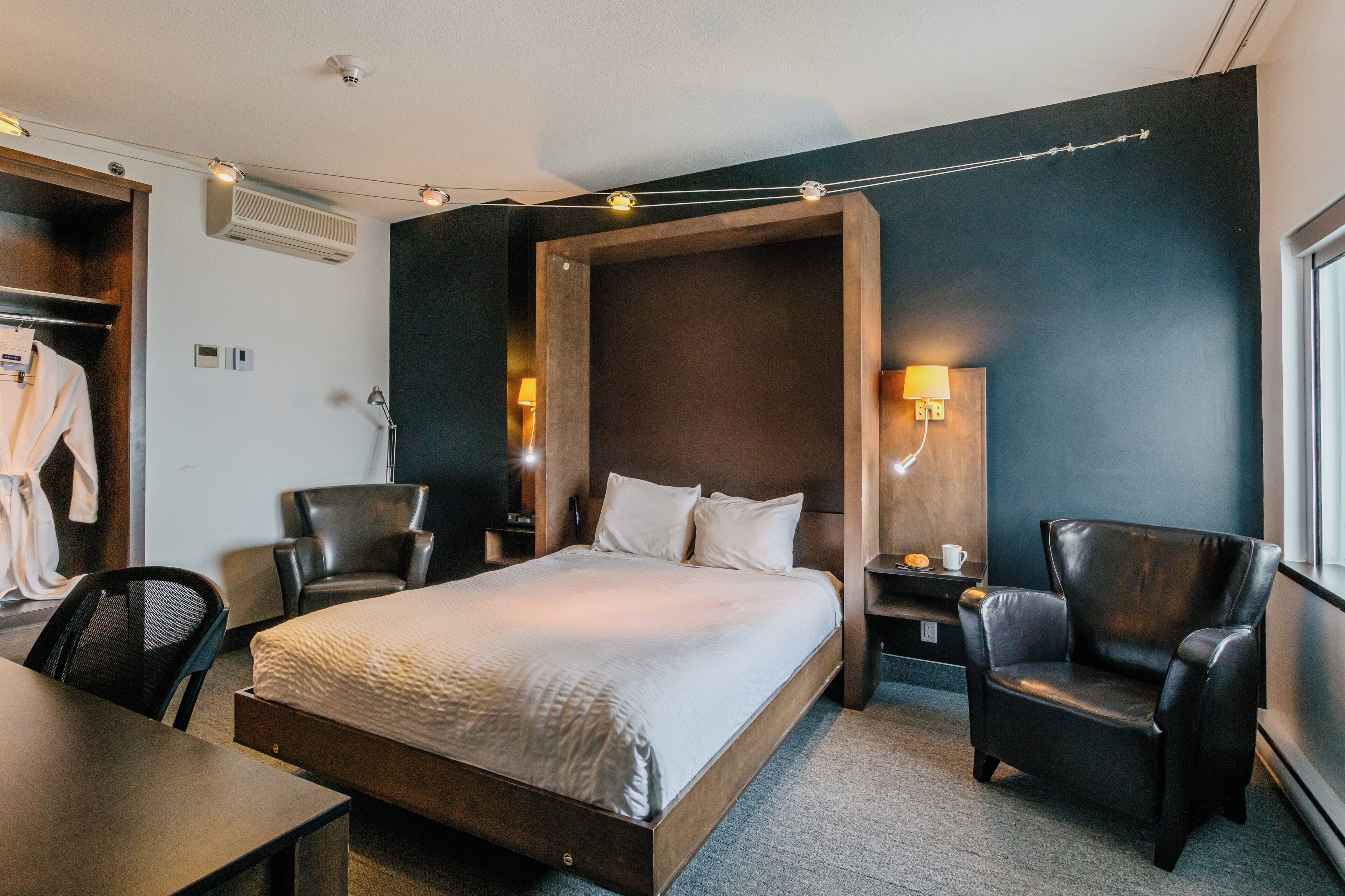Een moderne hotelkamer met een groot bed, twee fauteuils, een bureau en een kledingkast.