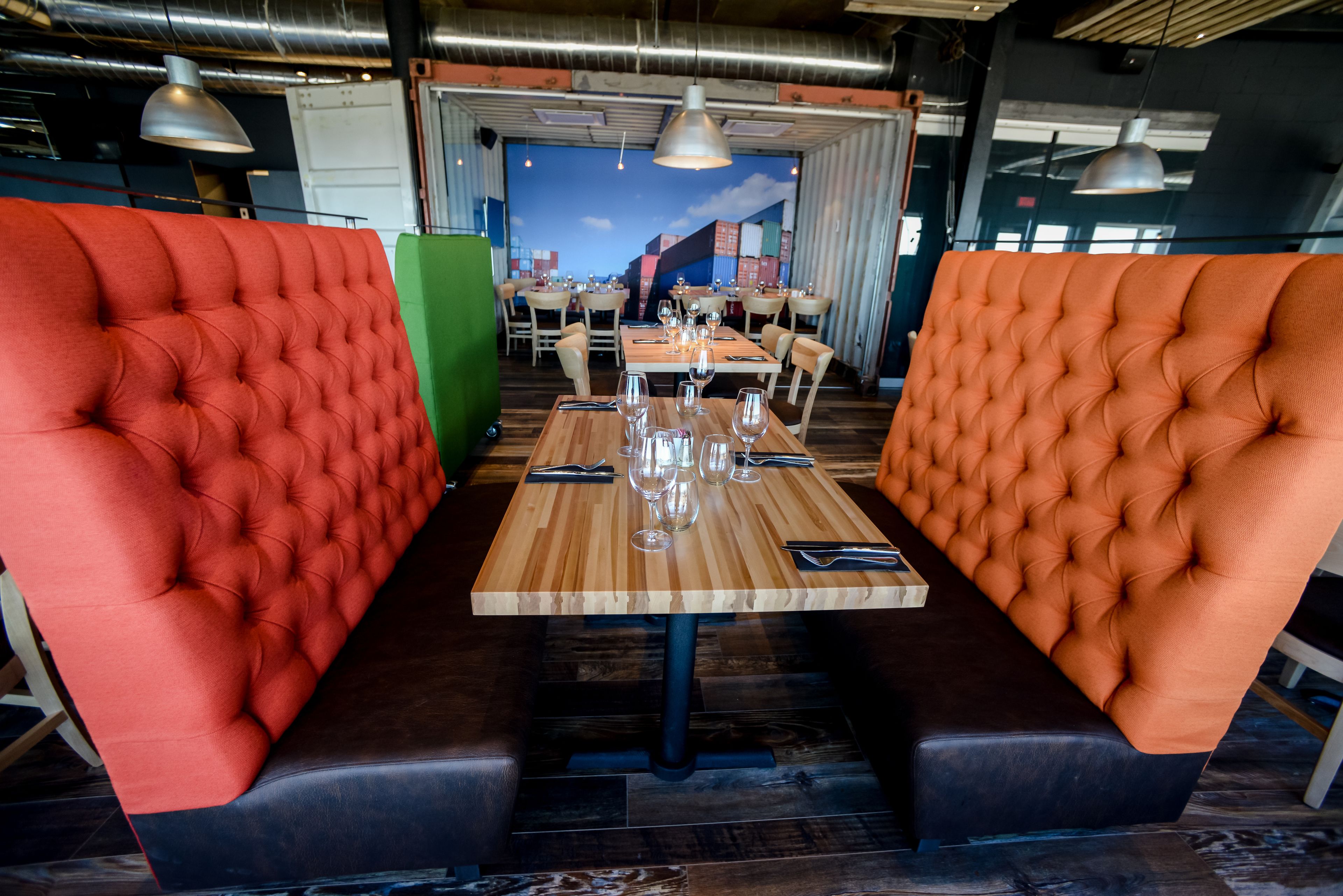 Een restaurant met rode en oranje gestoffeerde banken, houten tafels en hangende pendelverlichting.
