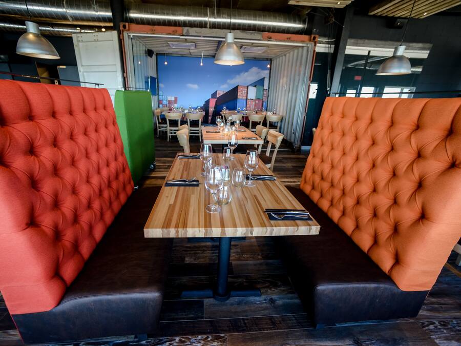 Een restaurant met rode en oranje gestoffeerde banken, houten tafels en hangende pendelverlichting.