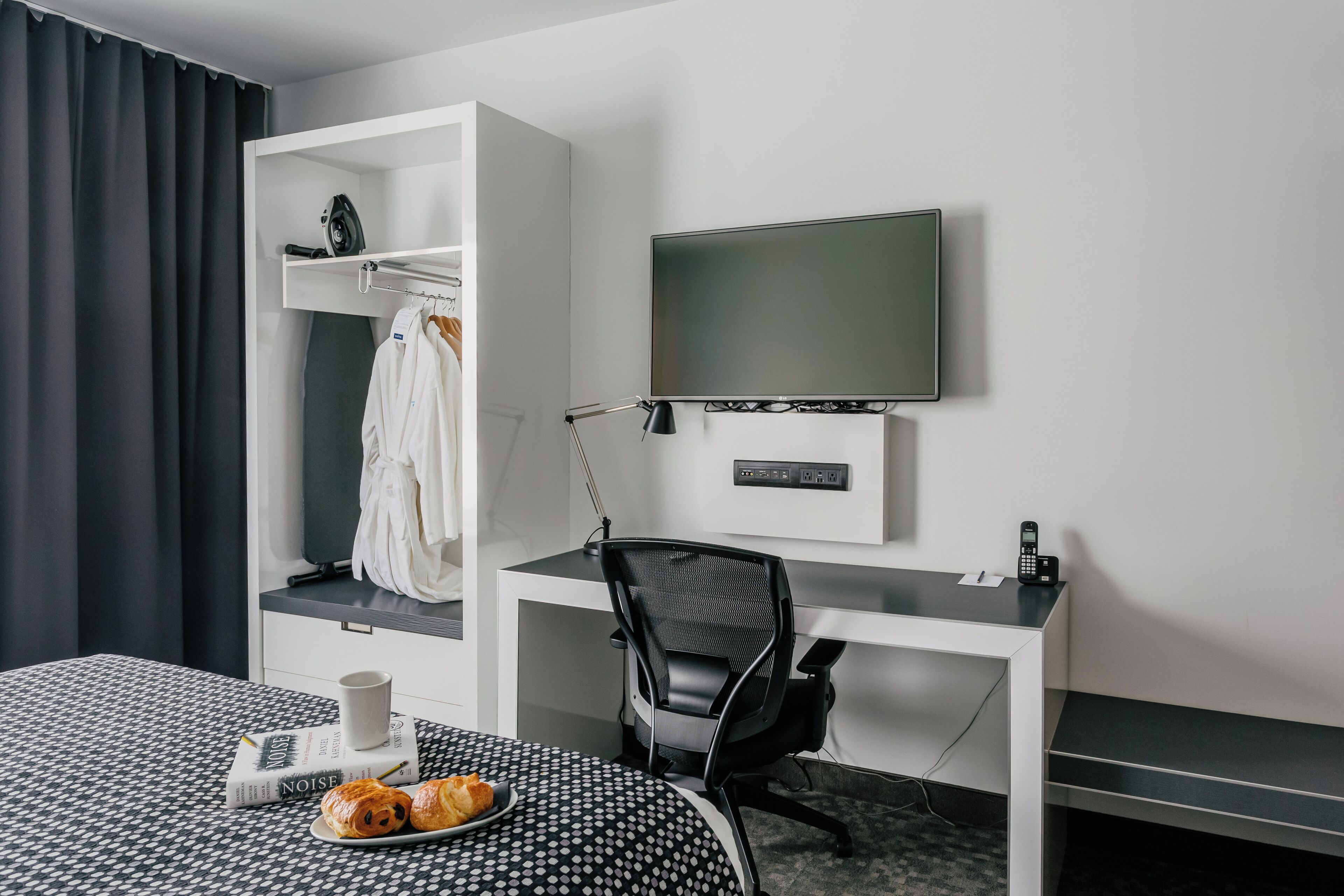 A hotel room with a bed, a desk with a chair, a TV, and a wardrobe.