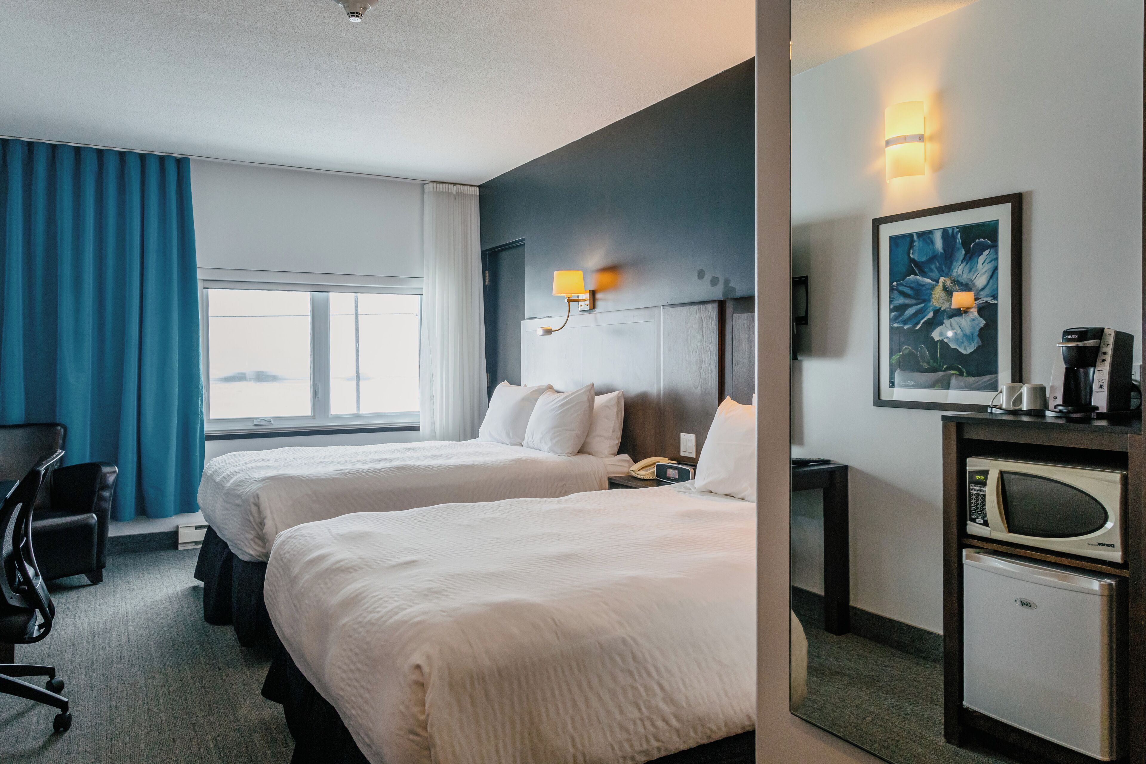 A hotel room with two beds, a desk, a chair, a microwave, and a coffee maker.