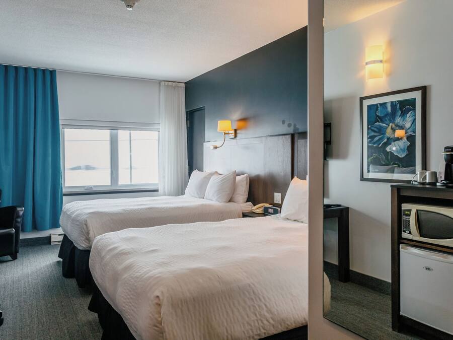A hotel room with two beds, a desk, a chair, a microwave, and a coffee maker.
