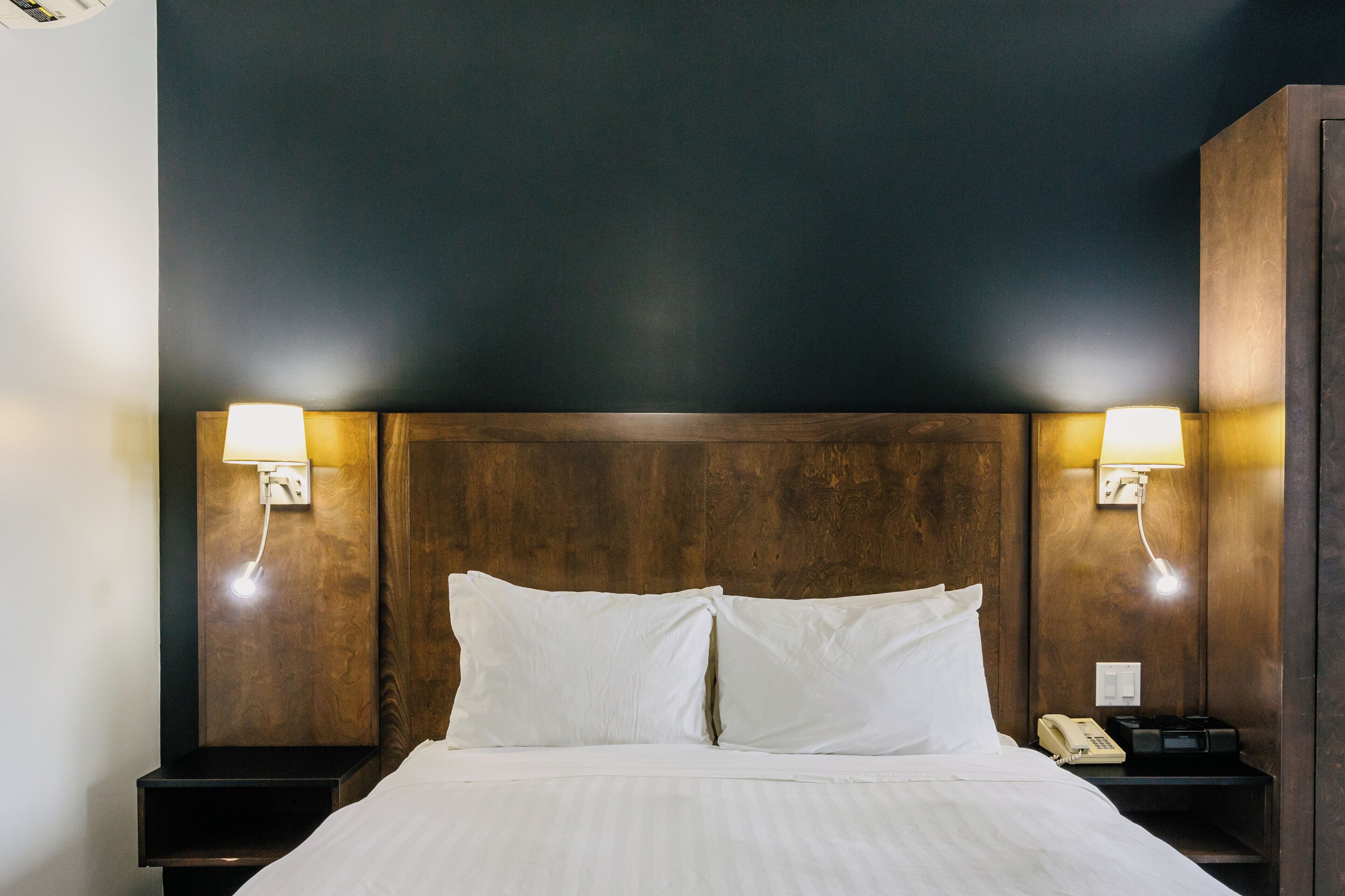 A hotel room with a wooden headboard, two bedside lamps, a telephone, and a neatly made bed.