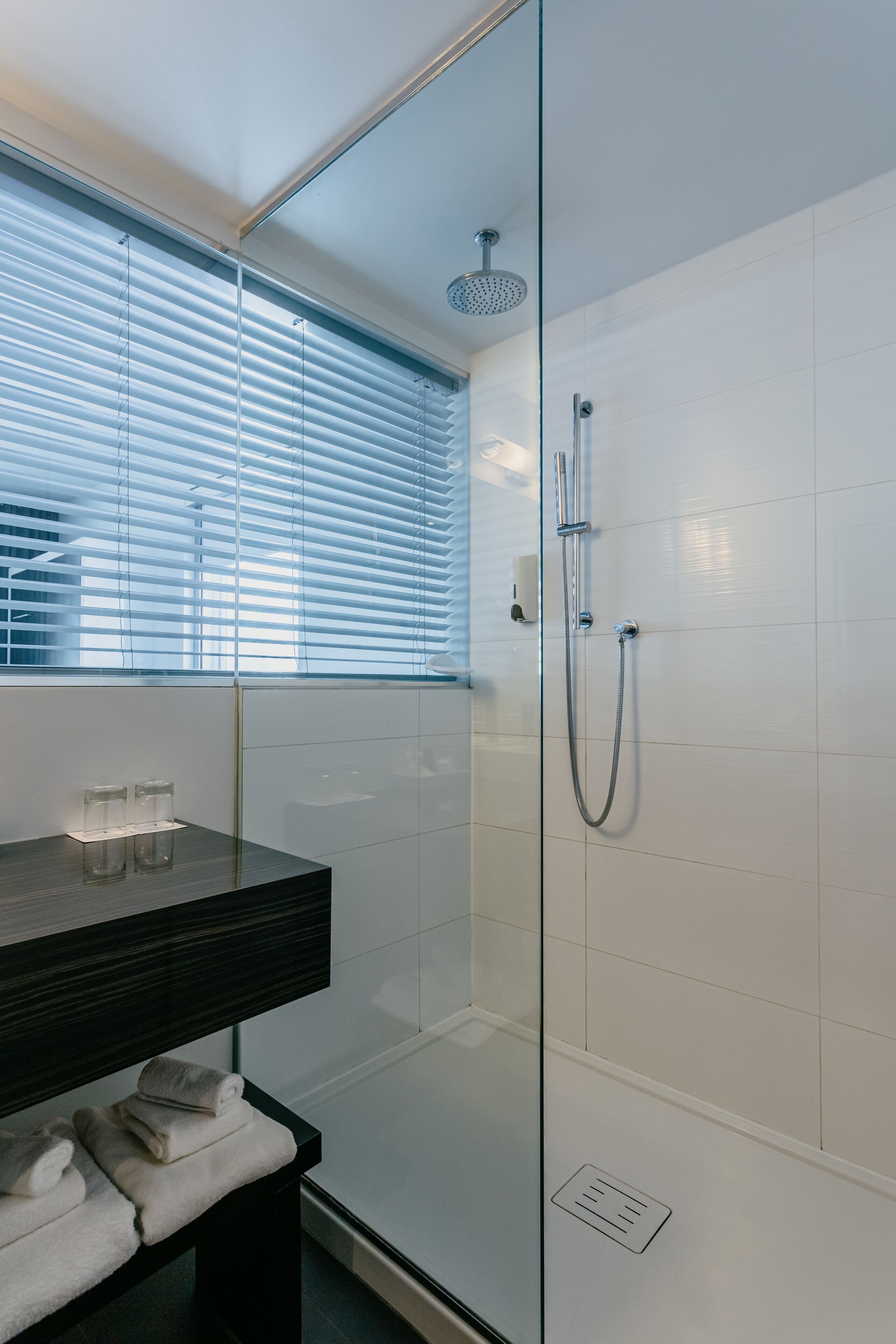 A modern bathroom with a glass shower enclosure, a black countertop with a glass container, and a towel rack.