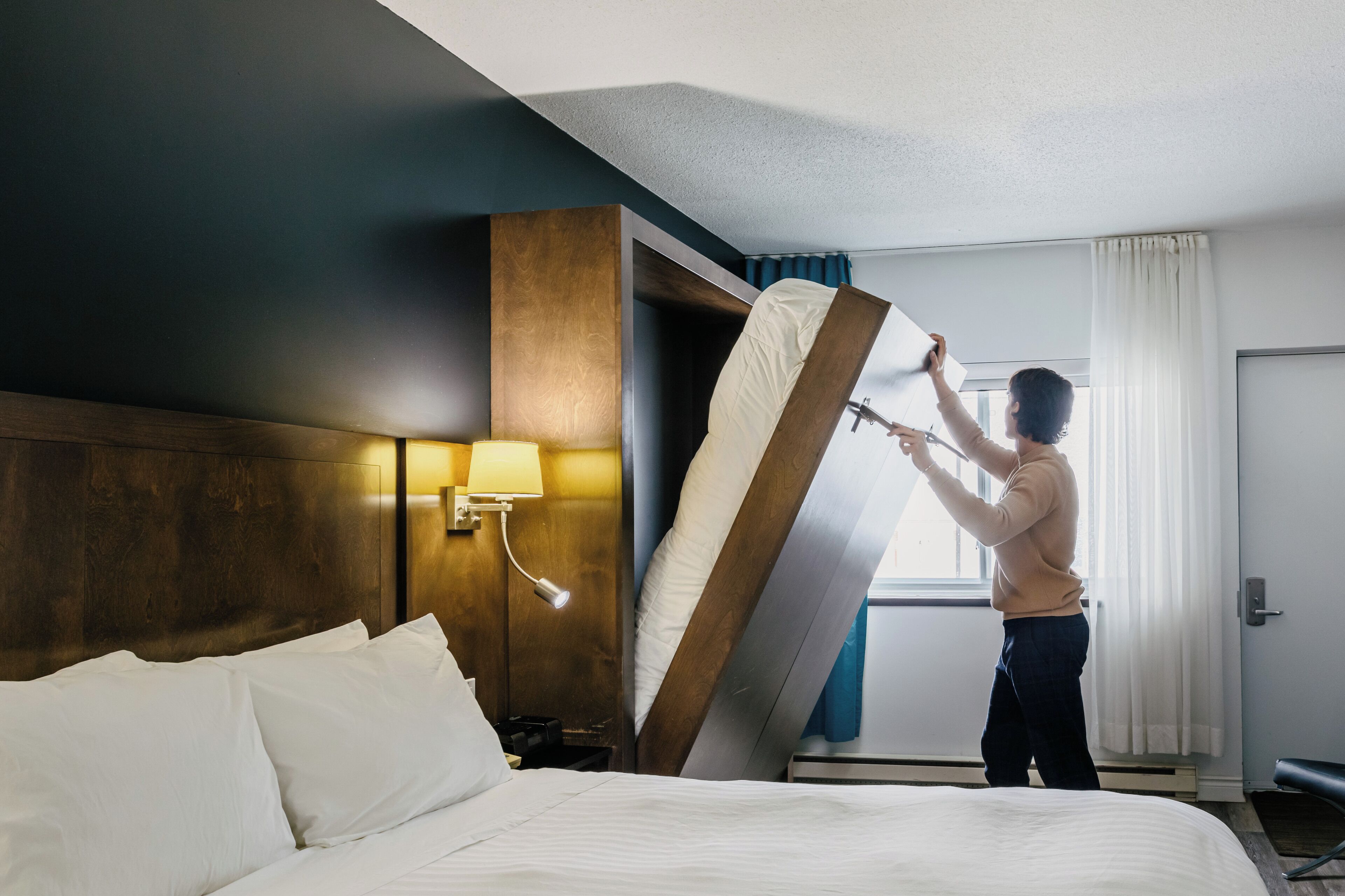 Une chambre d’hôtel avec un lit, une table de chevet avec une lampe et une fenêtre avec des rideaux.