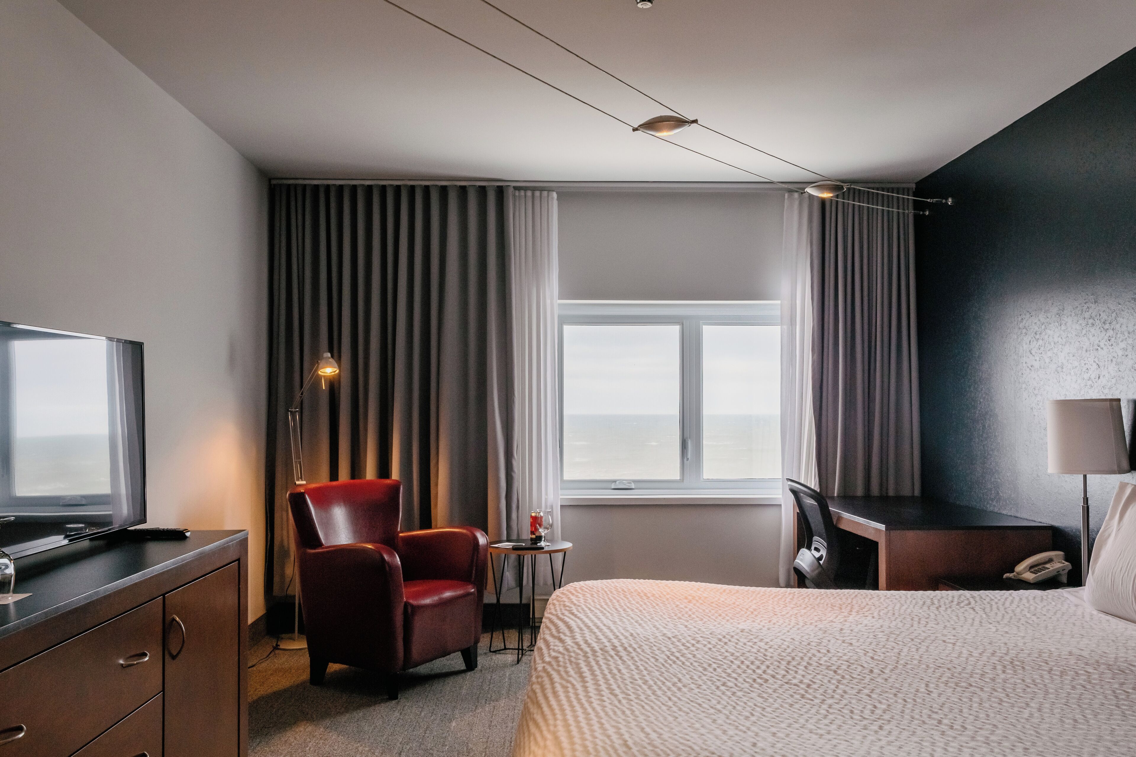 A hotel room with a bed, a desk, a chair, a TV, and a window with curtains.