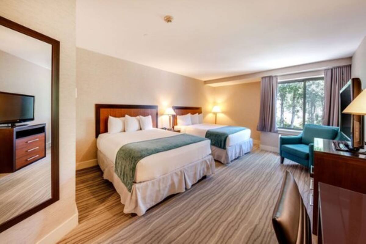 A hotel room with two beds, a desk, a television, and a window with curtains.