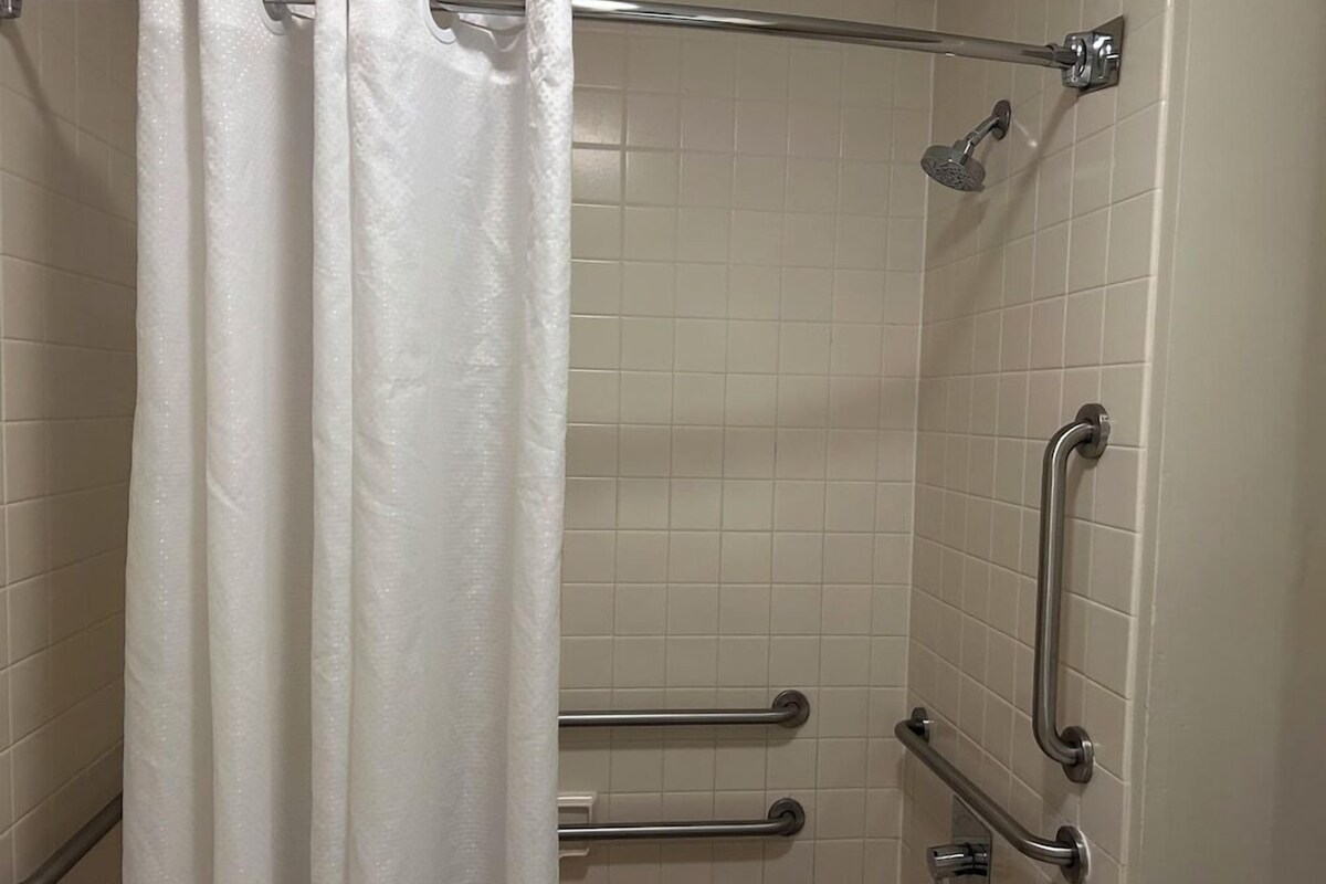 A shower with a white curtain, tiled walls, and metal grab bars.